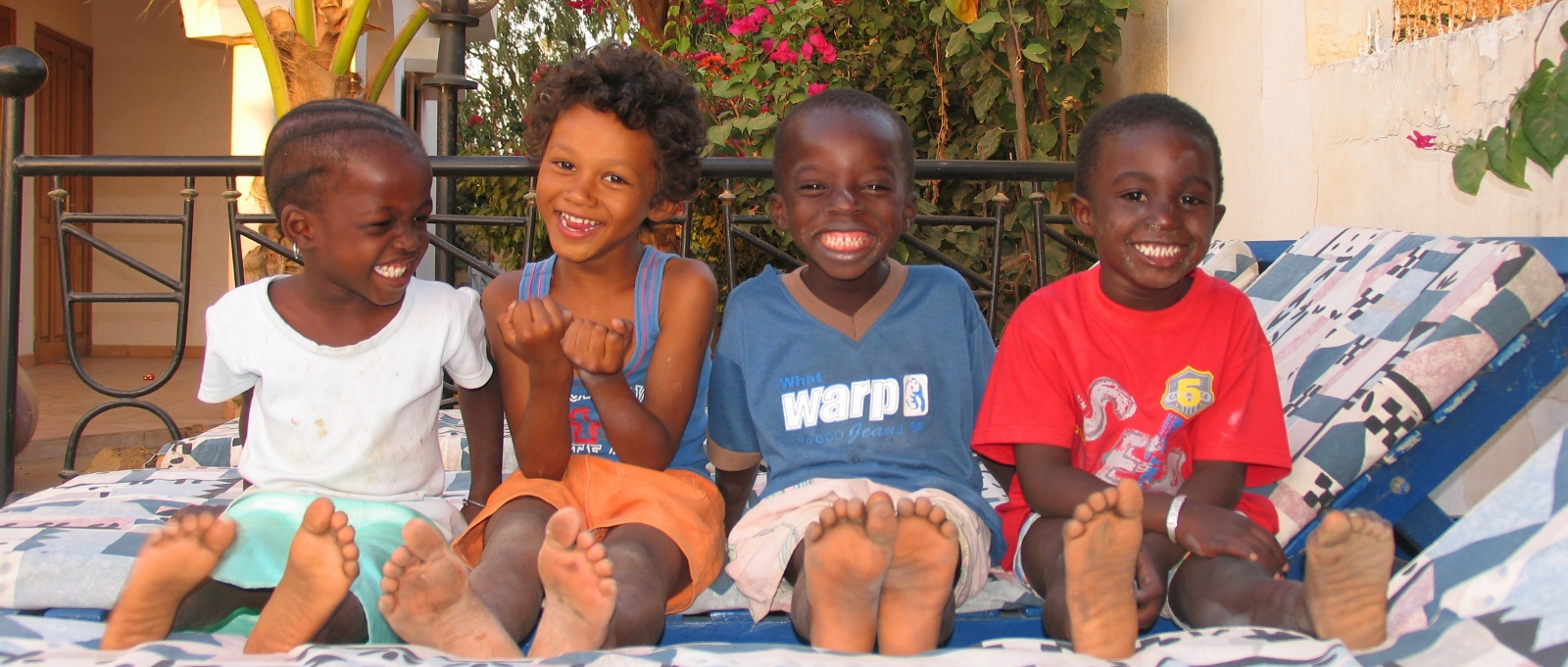 vier jonge Senegalese kindjes die op een ligstoel zitten, lachend voor de foto
